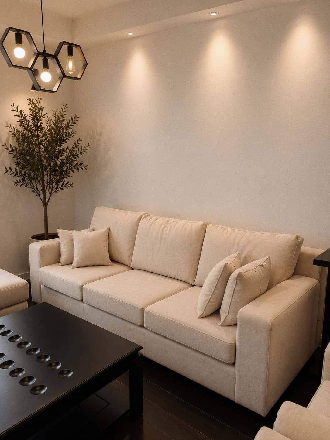 An NDB cream sofa beneath a hexagon pendant, with an olive tree and dimpled black coffee table in a Kigali lounge.