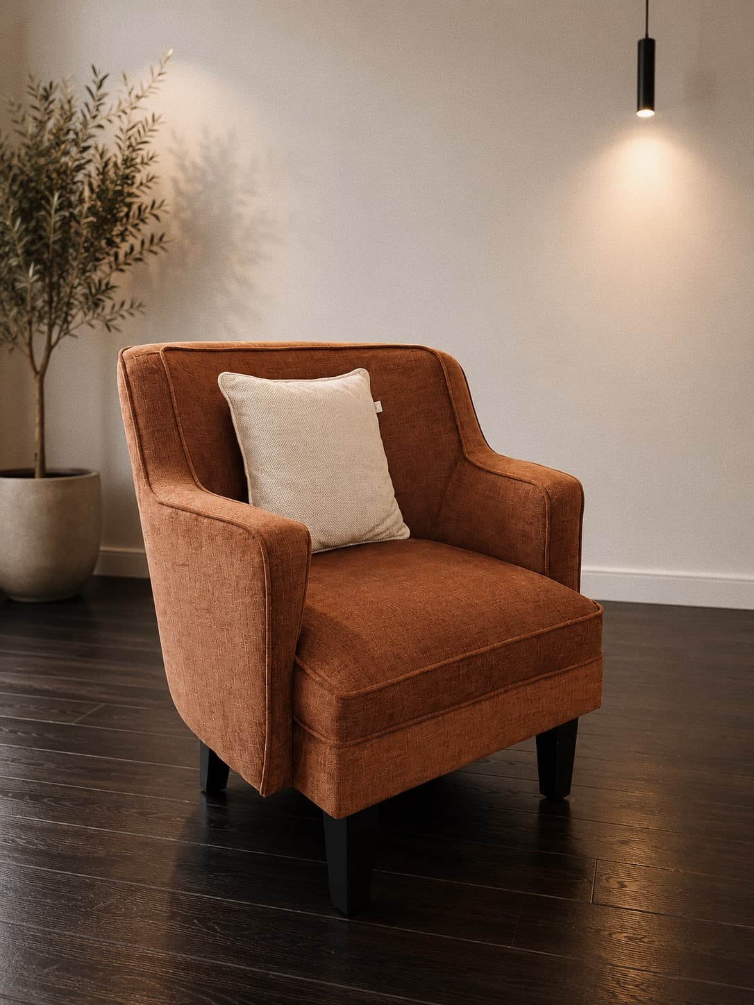 A rust velvet NDB armchair with a cream cushion beside an olive tree, under a pendant light.