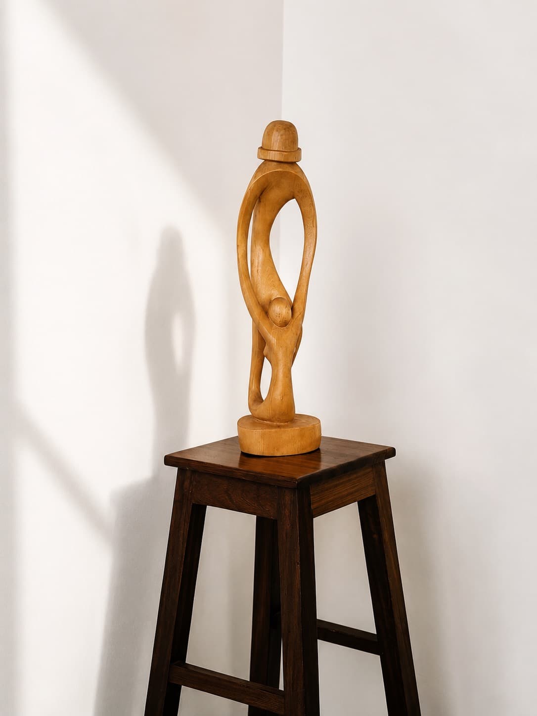 Hand-carved abstract wooden sculpture on a tall wooden stand.