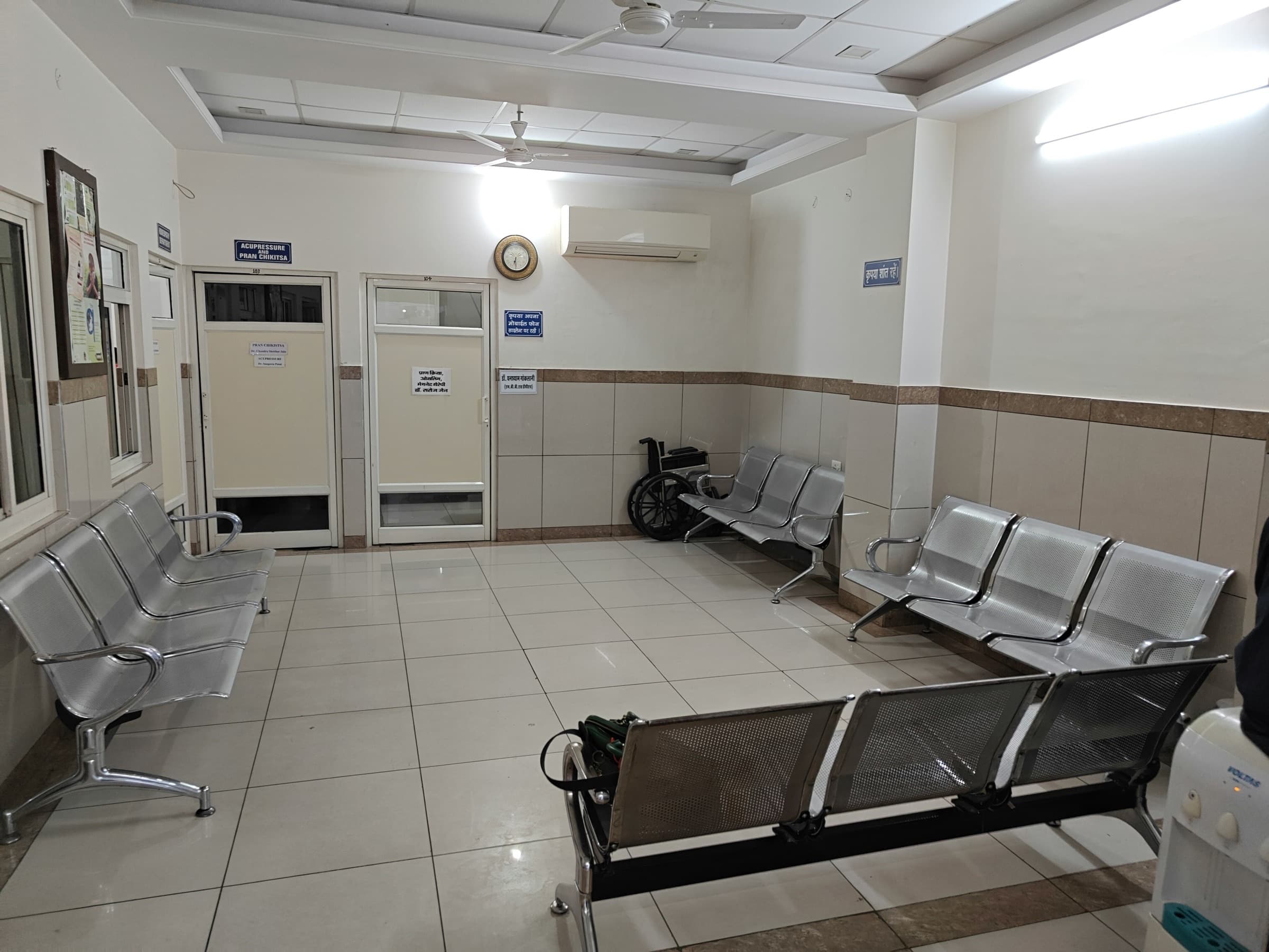 A clinic waiting area with rows of steel bench seating along tiled walls.
