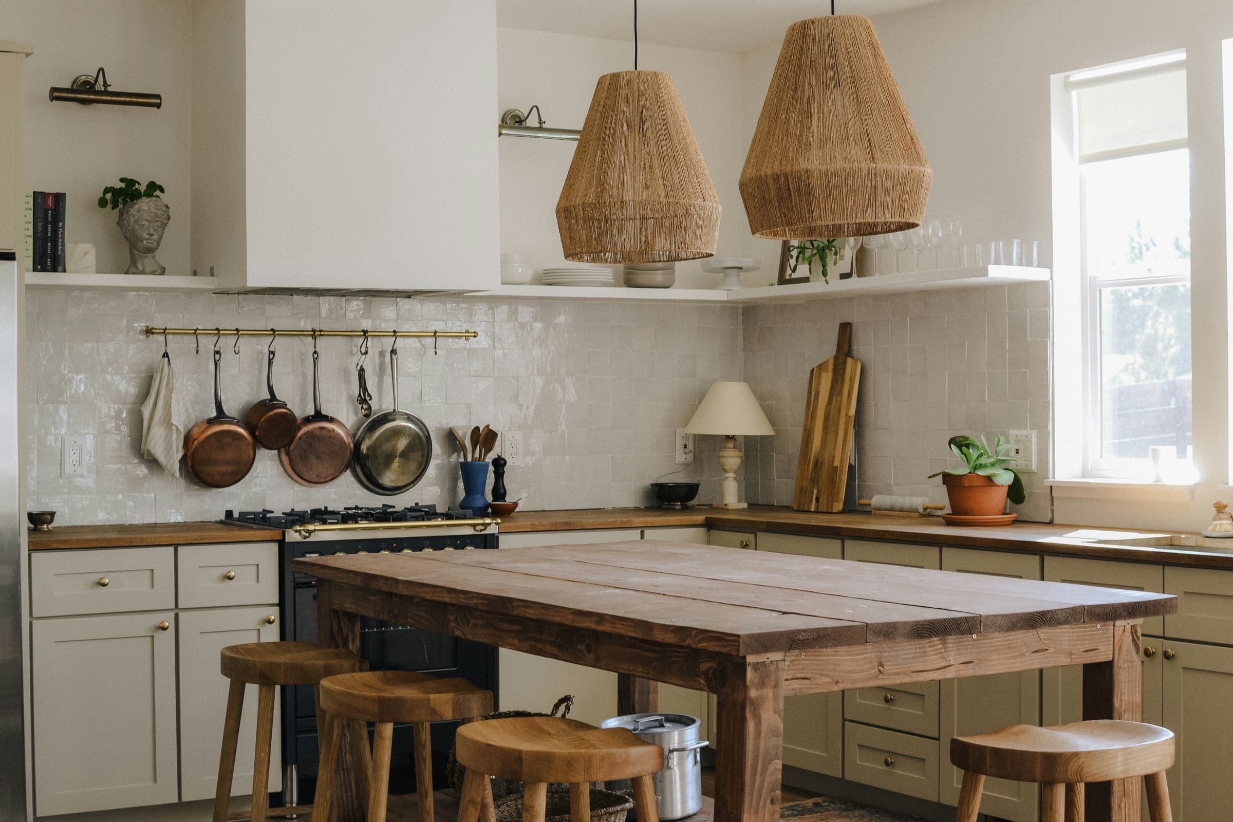 A warm kitchen with sage cabinetry, butcher-block counters, a timber island and jute pendants.