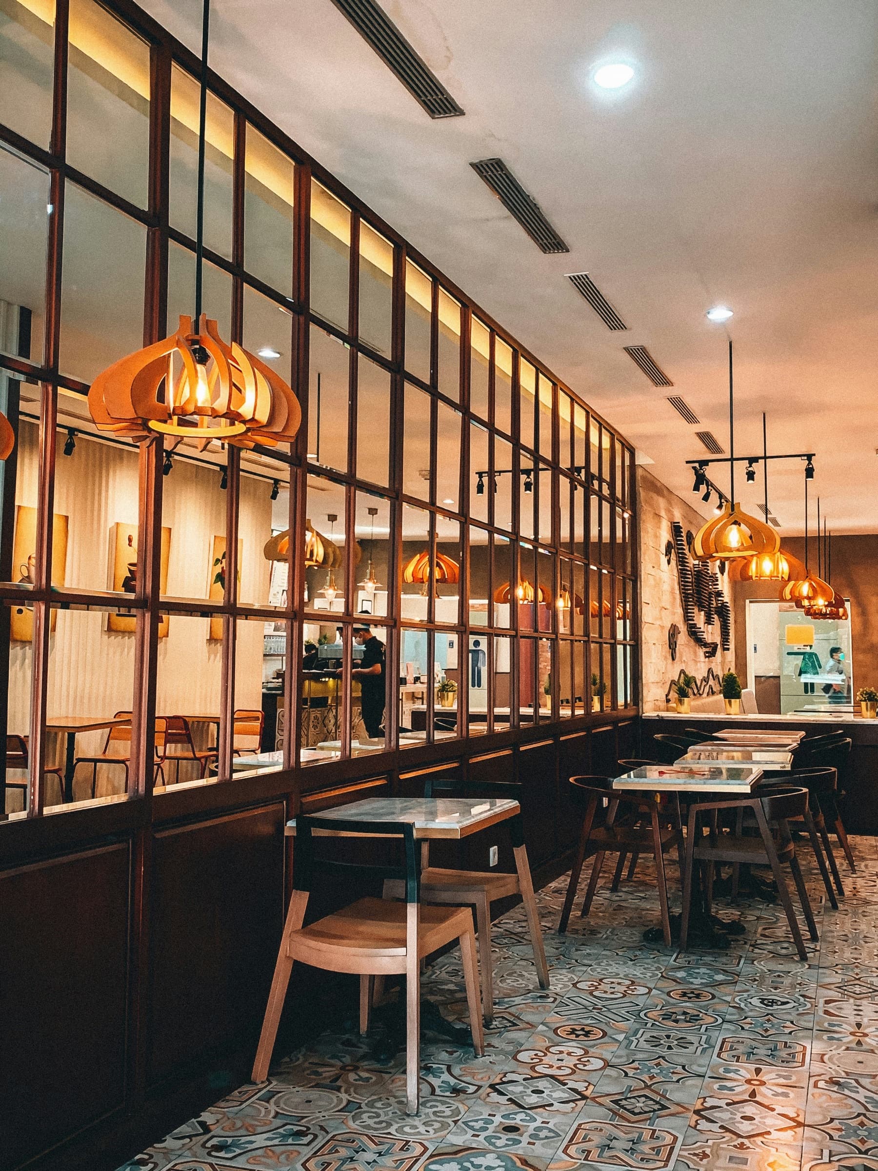 A restaurant interior with patterned tiled floor, marble-topped tables and carved timber pendants.